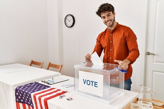 Young hispanic man smiling confident putting vote in box at electoral college