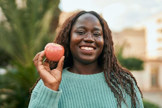 Young african woman smiling happy holding fresh red apple at the city