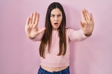 Obraz na płótnie Canvas Young brunette woman standing over pink background doing stop gesture with hands palms, angry and frustration expression