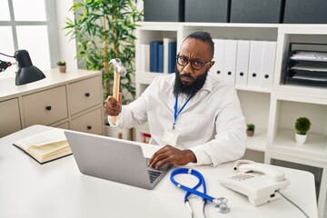 African american man working at medical clinic holding hammer thinking attitude and sober expression looking self confident