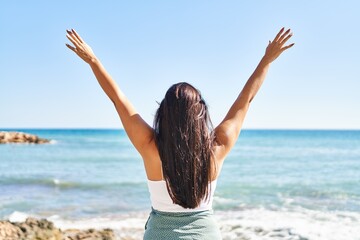 Young hispanic woman on back view with arms raised up at seaside