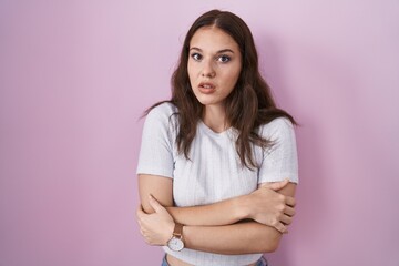 Fototapeta premium Young hispanic girl standing over pink background shaking and freezing for winter cold with sad and shock expression on face