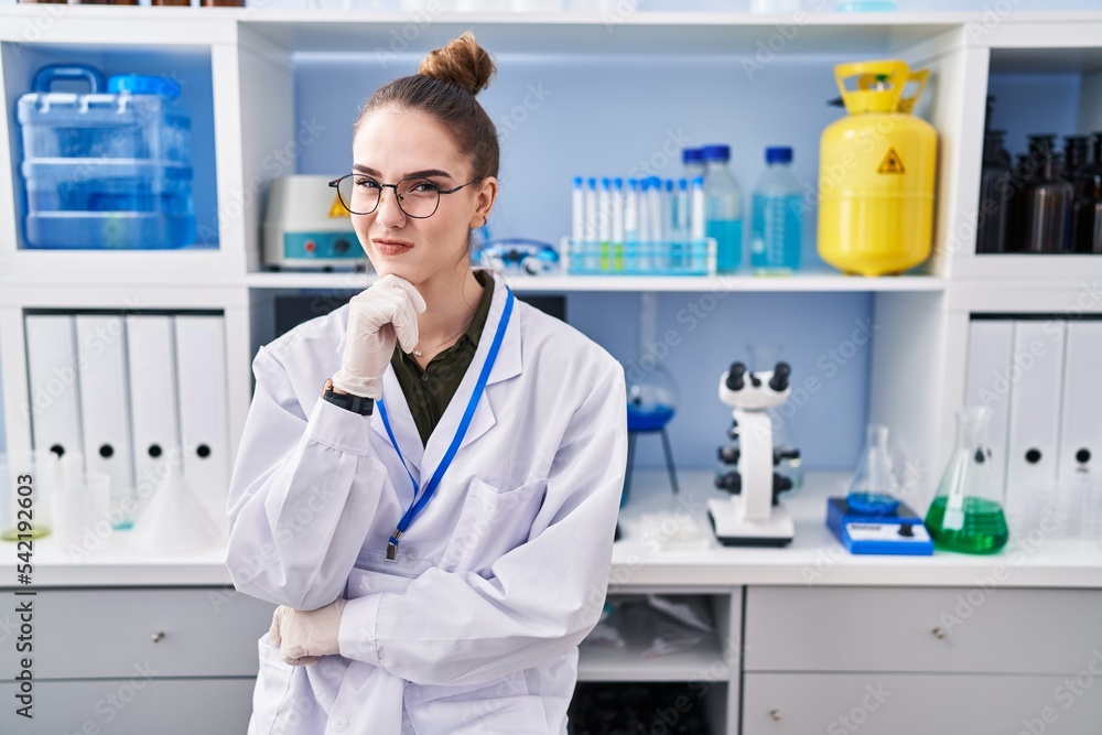 Wall mural Young hispanic girl working at scientist laboratory thinking concentrated about doubt with finger on chin and looking up wondering