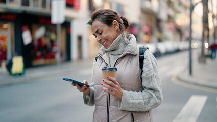 Obraz premium Middle age hispanic woman using smartphone drinking coffee at street