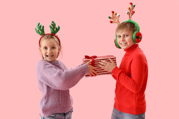 Happy little children in reindeer horns with Christmas gift on pink background