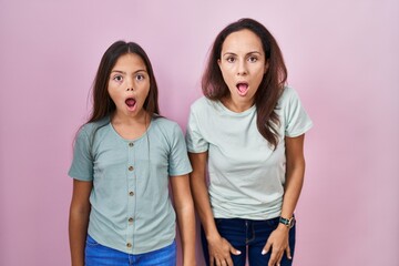 Young mother and daughter standing over pink background afraid and shocked with surprise and amazed expression, fear and excited face.