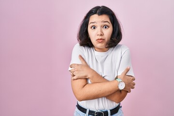 Young hispanic woman wearing casual white t shirt over pink background shaking and freezing for...
