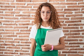 Young caucasian woman holding art notebook puffing cheeks with funny face. mouth inflated with air, crazy expression.