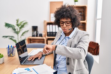 Black woman with curly hair wearing call center agent headset at the office checking the time on wrist watch, relaxed and confident