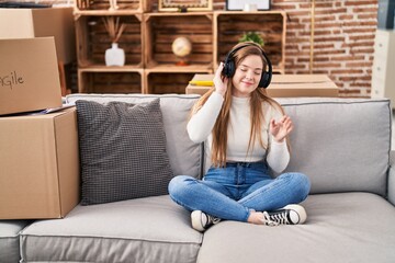 Obraz premium Young blonde woman listening to music sitting on sofa at new home