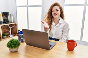 Young caucasian woman working at the office using computer laptop smiling cheerful offering palm...