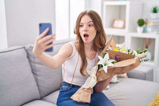 Caucasian woman holding bouquet of white flowers taking a selfie picture afraid and shocked with surprise and amazed expression, fear and excited face.