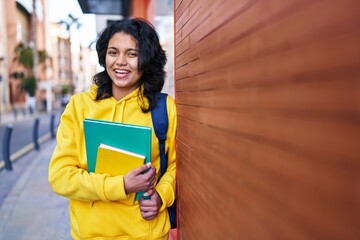 Young latin woman student smiling confident holding books at street