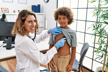 Mother and son wearing doctor uniform auscultating child chest at clinic