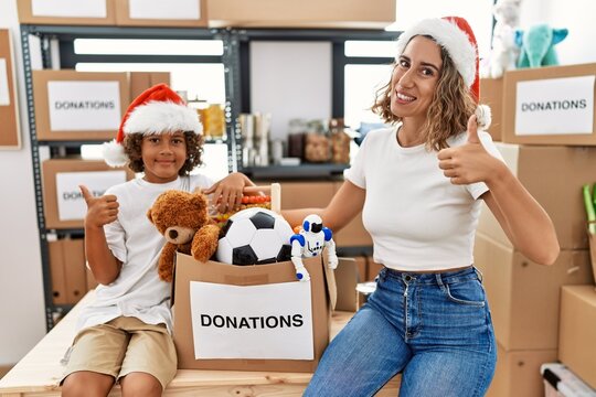 Young mother with little son wearing christmas hat at donations stand smiling happy and positive, thumb up doing excellent and approval sign