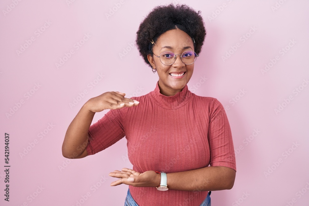 Poster Beautiful african woman with curly hair standing over pink background gesturing with hands showing big and large size sign, measure symbol. smiling looking at the camera. measuring concept.