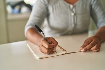 African american woman writing on notebook sitting on table at home