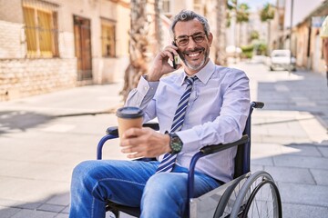 Middle age hispanic man sitting on wheelchair talking on the smartphone at street