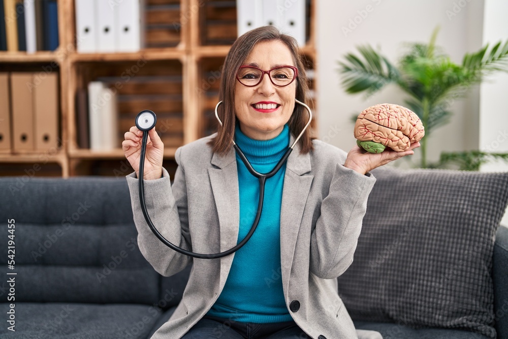 Poster Middle age hispanic woman working at therapy office holding brain smiling with a happy and cool smile on face. showing teeth.