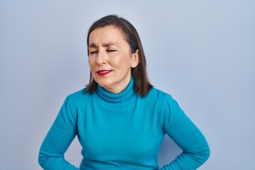 Middle age hispanic woman standing over isolated background with hand on stomach because indigestion, painful illness feeling unwell. ache concept.