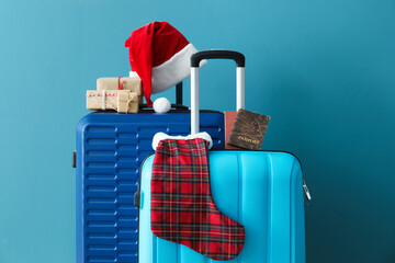 Suitcases with Santa hat, passports and Christmas gifts near blue wall