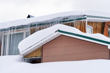 Icicles on roof of wooden private house resulting from improper construction of roof. Metal...