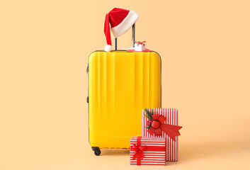 Suitcase with Santa hat and Christmas gifts on beige background