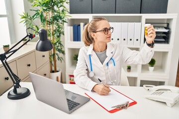 Young blonde woman wearing doctor uniform prescribe pills at clinic