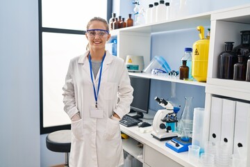 Naklejka premium Young blonde woman wearing scientist uniform standing at laboratory