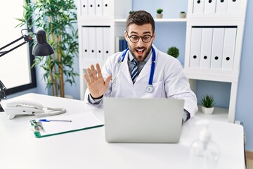 Young hispanic man wearing doctor uniform having video call at clinic