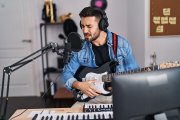 Young hispanic man singing song playing electric guitar at music studio