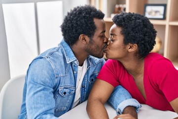 African american man and woman couple sitting on table kissing at home