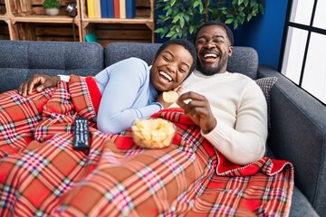 Young african american couple sitting on the sofa watching tv smiling and laughing hard out loud...