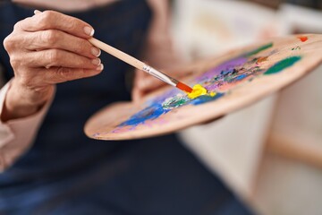 Middle age woman artist mixing color on palette at art studio