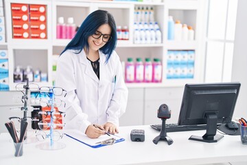 Young caucasian woman pharmacist smiling confident writing on document at pharmacy