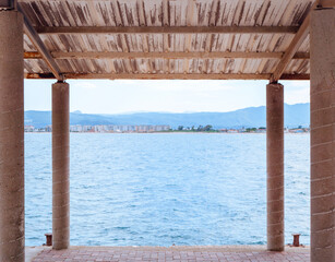 Fototapeta na wymiar View on a blue sea from under an awning on a small concrete pier