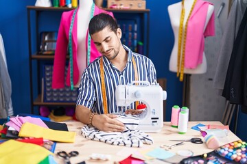 Fototapeta premium Young hispanic man tailor smiling confident using sewing machine at sewing studio