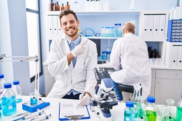 Hispanic man and woman working at scientist laboratory smiling happy pointing with hand and finger to the side