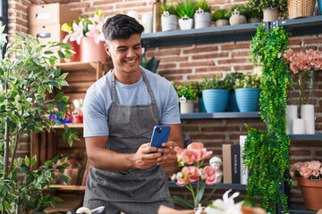 Fototapeta na wymiar Young hispanic man florist make photo to plant by smartphone at flower shop