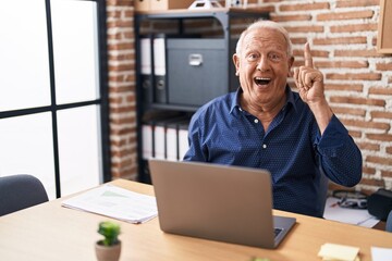 Fototapeta premium Senior man with grey hair working using computer laptop at the office pointing finger up with successful idea. exited and happy. number one.