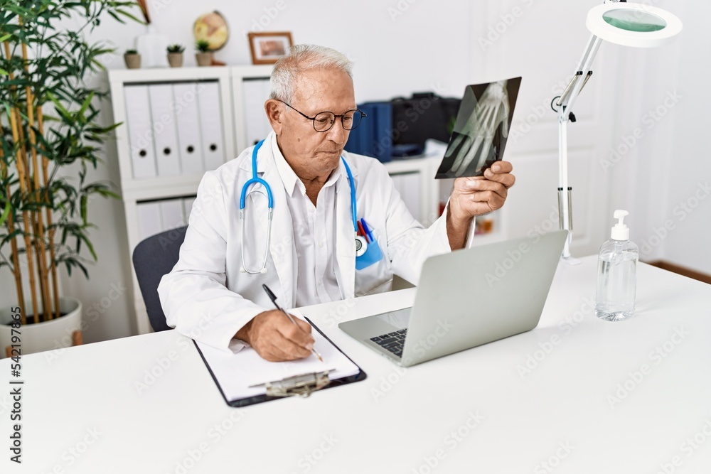 Sticker Senior man wearing doctor uniform holding xray working at clinic