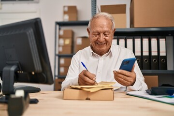 Senior man ecommerce business worker writing on package using smartphone at office