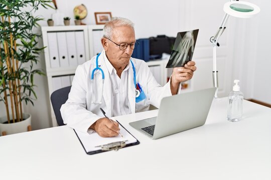 Senior man wearing doctor uniform holding xray working at clinic