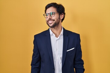 Handsome latin man standing over yellow background looking away to side with smile on face, natural expression. laughing confident.