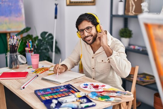 Young hispanic man artist listening to music drawing on notebook at art studio