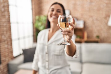 Young beautiful hispanic woman drinking glass of wine standing at home