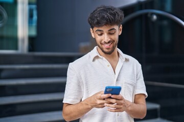 Young arab man smiling confident using smartphone at street