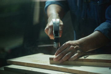 A carpenter furniture maker hammers a nail into the back of the cabinet with a hammer