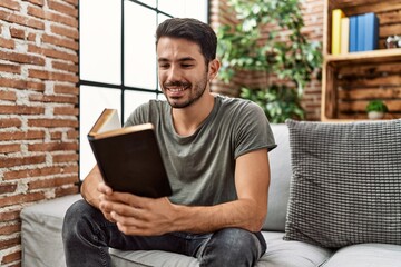 Young hispanic man smiling confident reading book at home