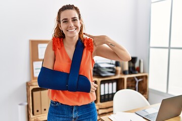 Young redhead woman wearing arm on sling at the office pointing finger to one self smiling happy...